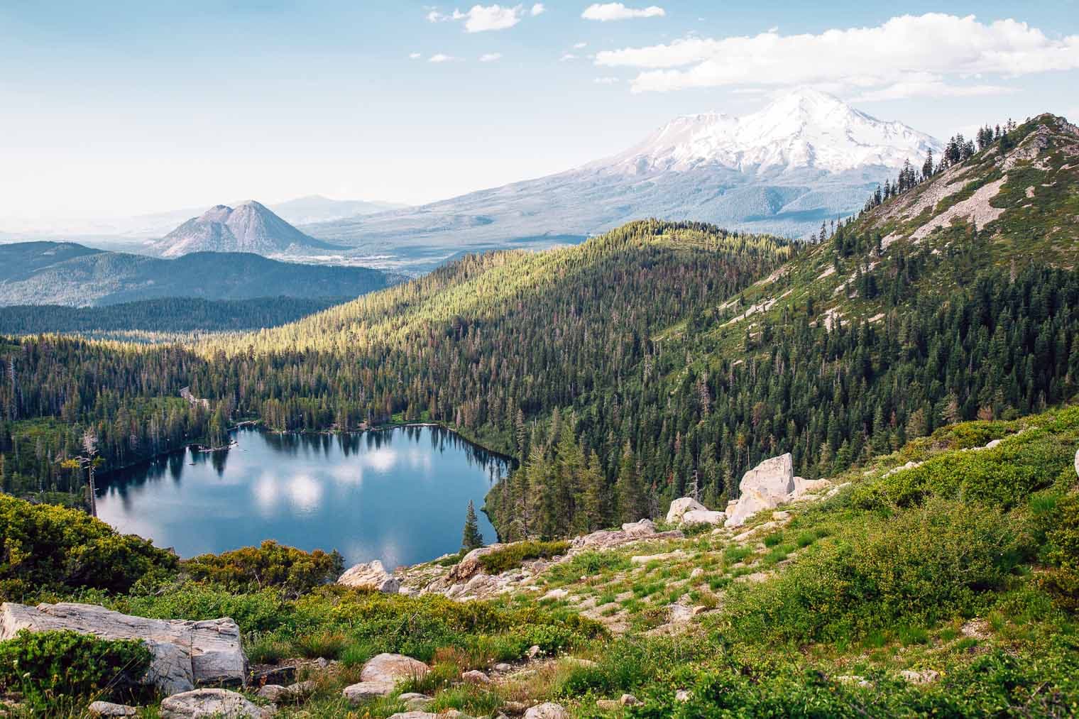 A serene landscape featuring a tranquil lake surrounded by lush forest and distant mountains.