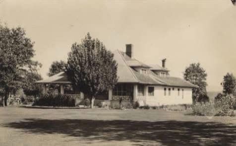 A historic, one-story house surrounded by trees and a lawn.