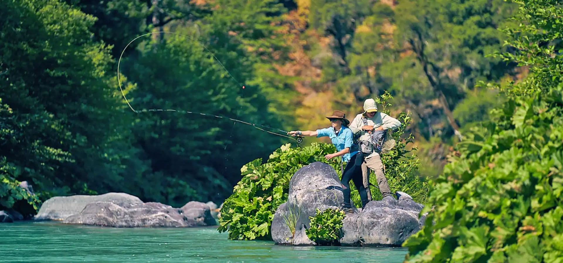 Two fishermen casting lines into a river surrounded by lush greenery.