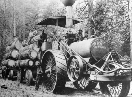 A vintage steam-powered logging locomotive transporting timber through a forest with workers on board.