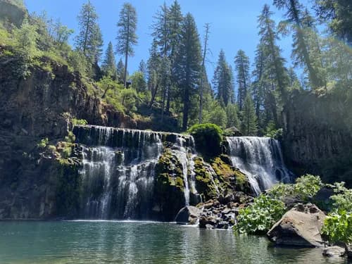 A serene waterfall cascading down rocky cliffs, surrounded by lush green trees and a clear pool below.
