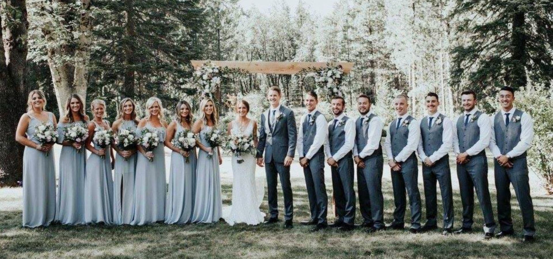 A wedding party poses in formal attire amidst a forest setting.