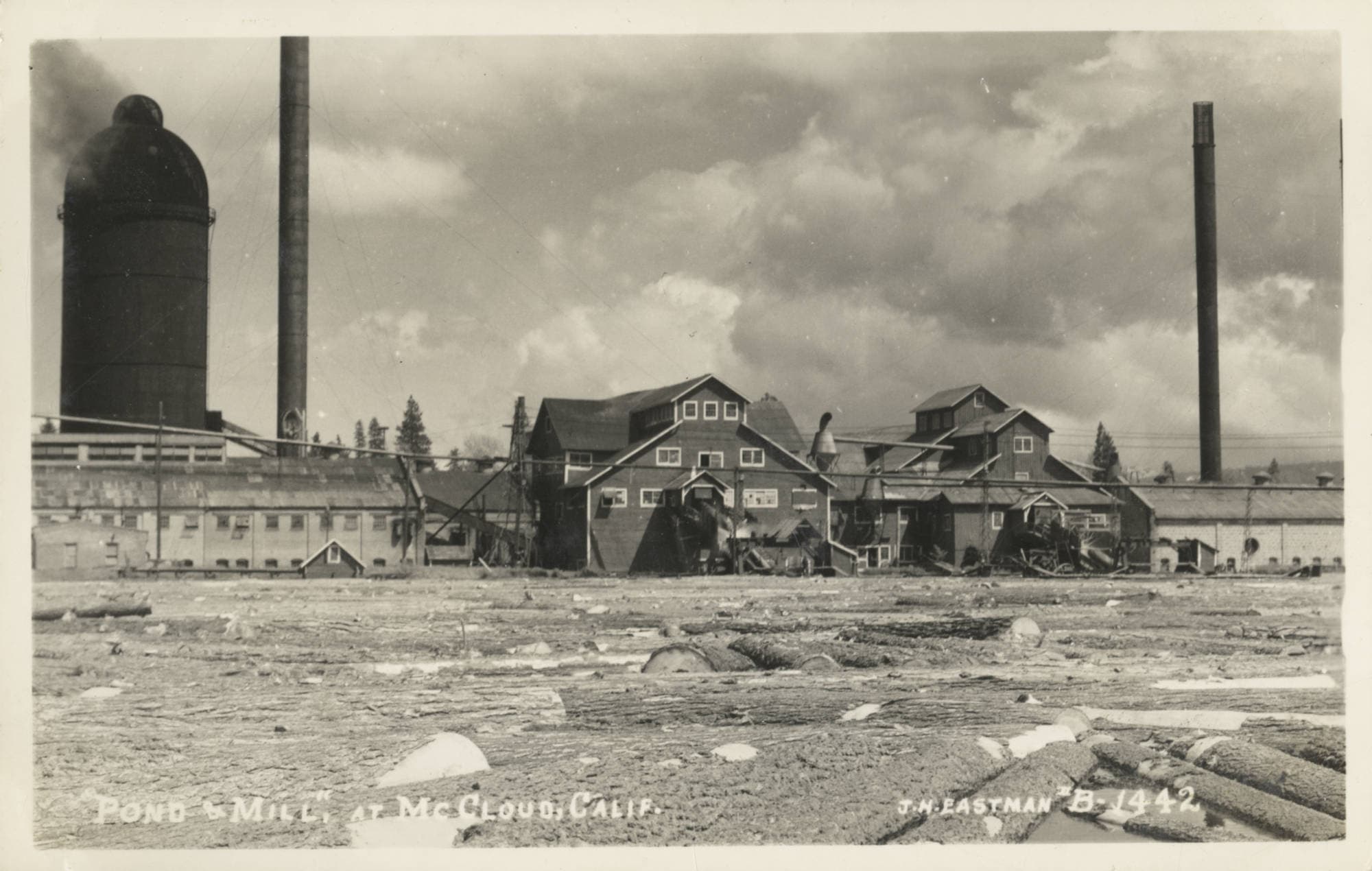 Black and white photograph of a lumber mill at McCloud, California, with large industrial buildings and smoke stacks.