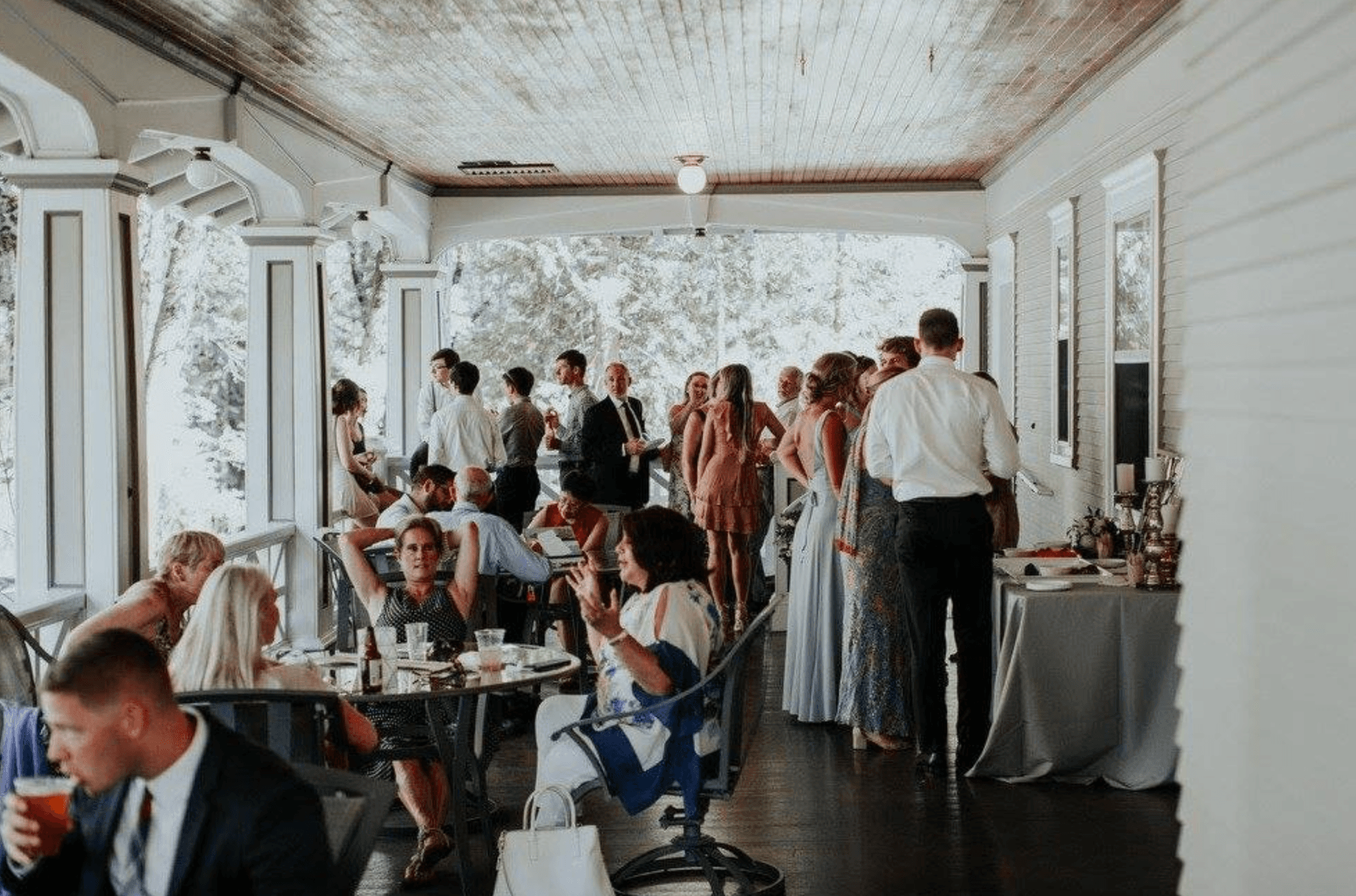A group of people socializing at a semi-outdoor event, with some seated at tables and others mingling.