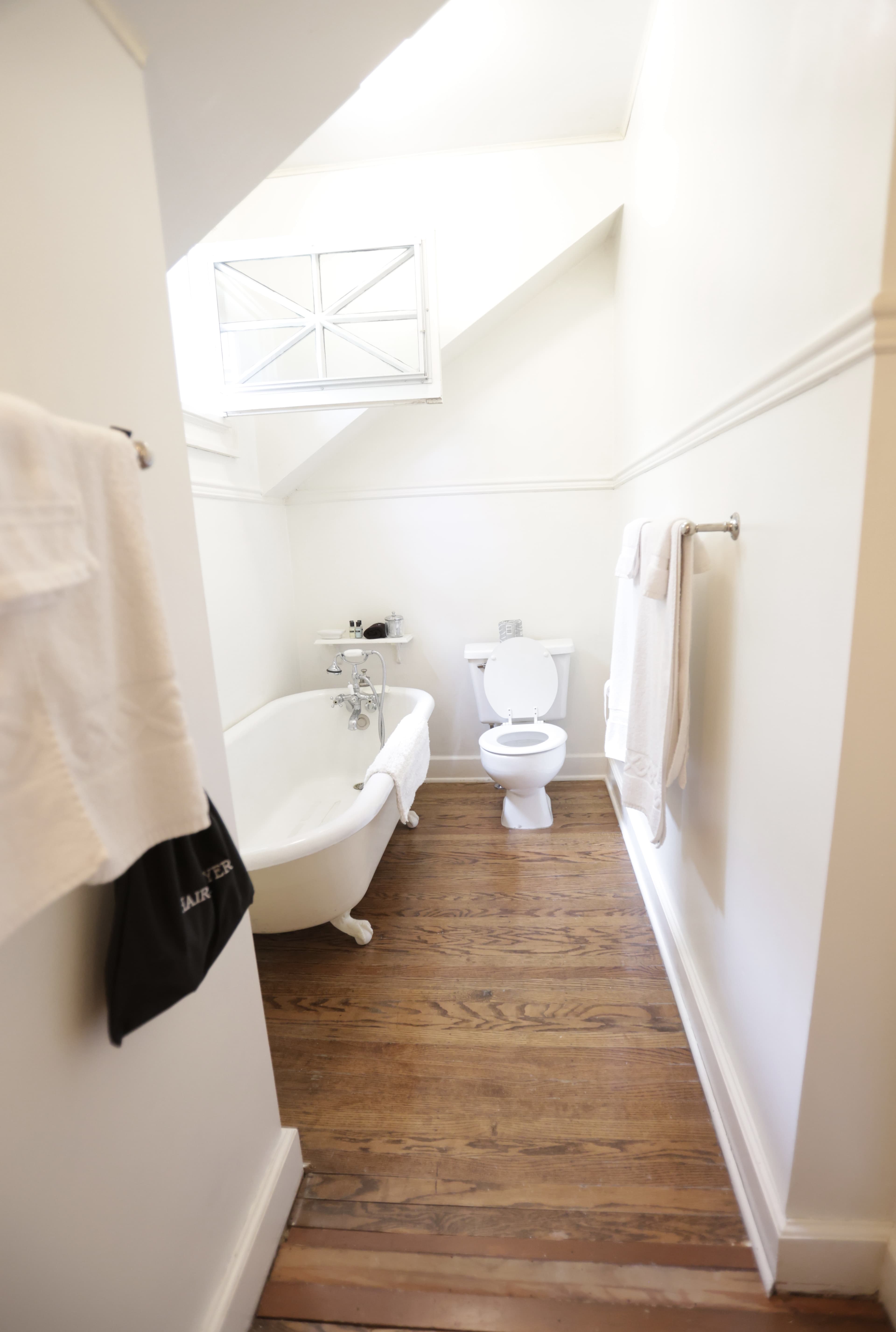 A clean, minimalist bathroom featuring a bathtub and toilet with wooden flooring.